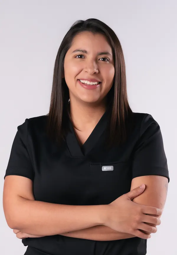 La Dra. Lourdes Alanis Naranjo, con uniforme quirúrgico negro y los brazos cruzados, sonríe a la cámara.