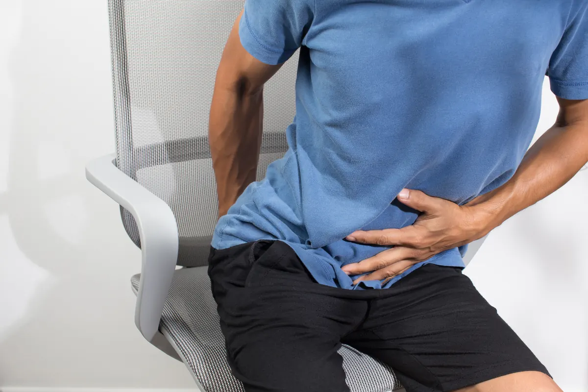 Hombre sentado se sujeta el abdomen con la mano por el dolor.