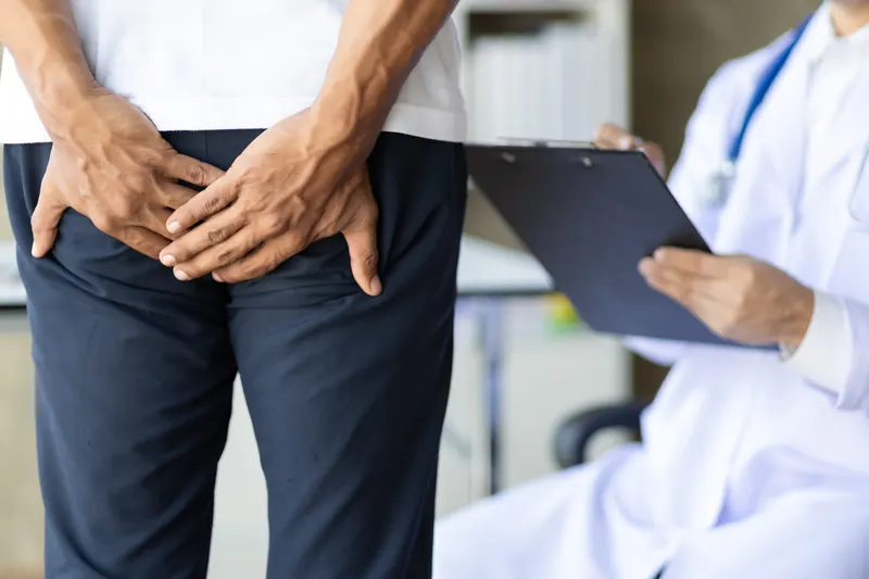 Hombre se sujeta la ingle con ambas manos mientras un médico toma notas en una tabla.